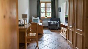Een kamer met een houten bureau, een stoel, een bank, een radiator en een raam met gordijnen.