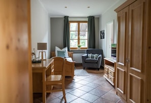 Una habitación con un escritorio de madera, una silla, un sofá, un radiador y una ventana con cortinas.
