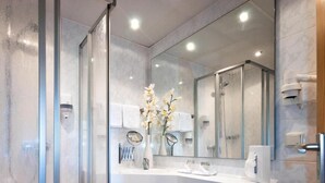 Een moderne badkamer met een douchecabine van glas, een wit wastafelmeubel met een spiegel, en een bloevas.