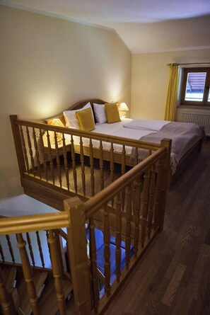 Een kamer met een houten trap, een bed met wit beddengoed en twee kussens, een bedlampje en een raam met gordijnen.