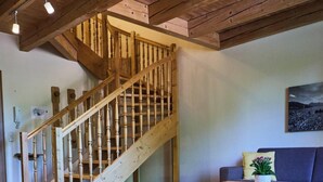 A wooden staircase leading to an upper level, a sofa, a small table with a plant, and a painting on the wall. - Der Tegernseer Hof (Gmund am Tegernsee)