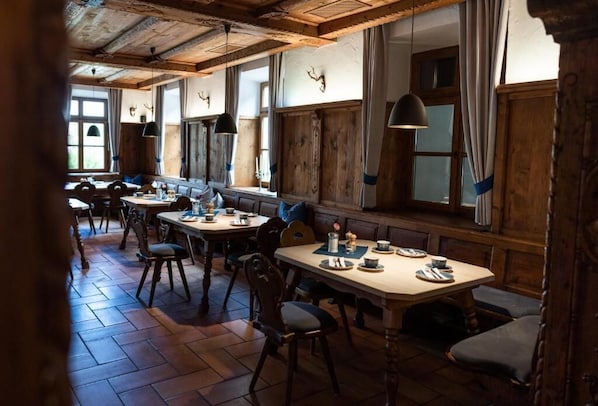 Un comedor rústico con mesas y bancos de madera, ventanas grandes con cortinas y techo de madera.