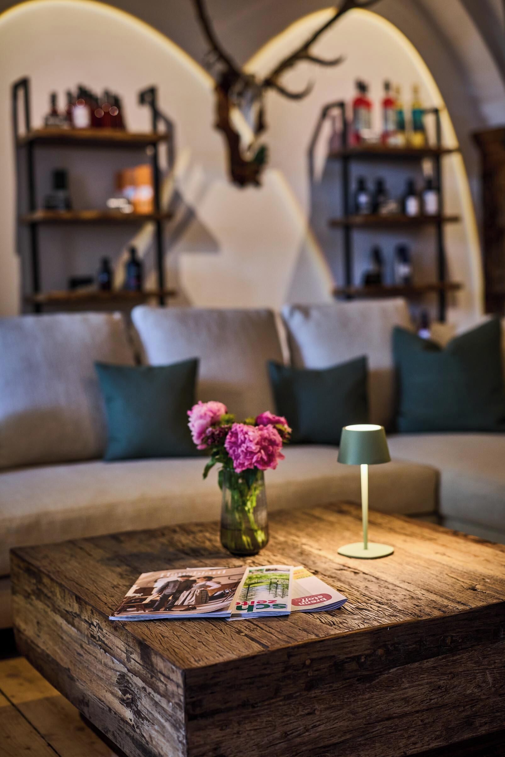 A cozy living area with a wooden coffee table, a vase with pink flowers, and a lamp.