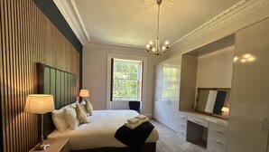 A bedroom with a bed, bedside lamps, a window, a wardrobe, and a mirror. - Crown Circus Three Bedroom Apartment (Hillhead)