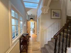 Ein Flur mit Oberlicht, Holzdielen, einem Tisch und einer Treppe.