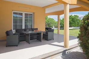 Une terrasse extérieure avec une table et des chaises, une grande fenêtre et une vue sur la verdure.