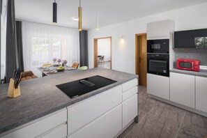 Une cuisine moderne avec un évier noir, des armoires blanches, un micro-ondes rouge et un coin repas comprenant une table et des chaises.