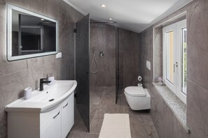 Une salle de bain moderne avec un grand miroir, un lavabo blanc, des toilettes et une cabine de douche.