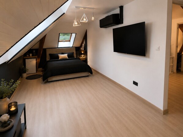 A modern bedroom with a skylight, a bed, a TV, and a small bedside table. - Vrbo Property (Le Mans)