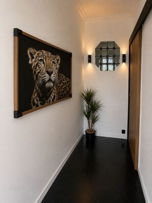 A hallway with a large framed picture of a leopard, a potted plant, and a wall-mounted light fixture. - Vrbo Property (Le Mans)