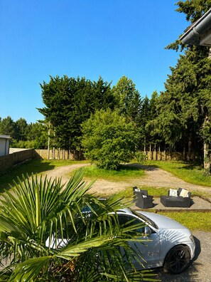 A white car parked in a driveway with a patio area and a large tree in the background. - Vrbo Property (Le Mans)