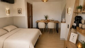 Een kleine hotelkamer met een bed, een eettafel, stoelen, een koffiezetapparaat en een klein kastje.