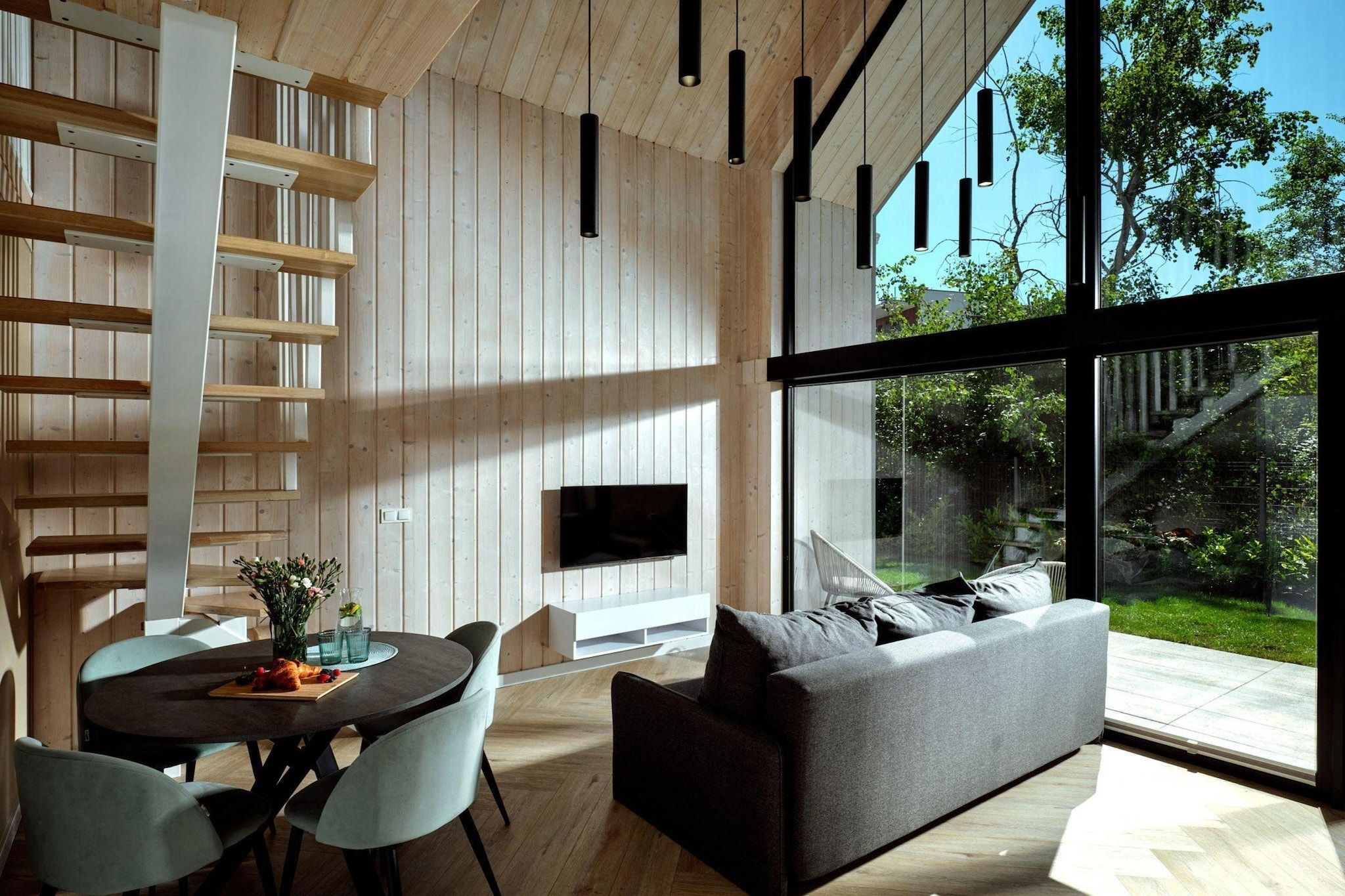 Uma sala de estar moderna com lareira, um sofá, uma mesa de jantar com cadeiras e uma grande janela com vista para o exterior.