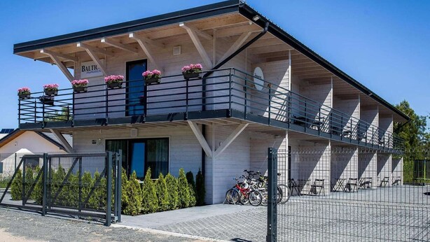 Un edificio de dos pisos con un balcón, un cartel que dice 'BALTIC MIELN' y una motocicleta estacionada afuera.