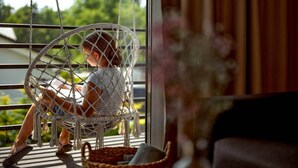 Una persona sentada en una silla de macramé junto a una ventana con vista a follaje exterior.