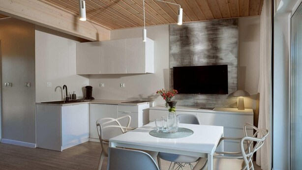 A modern kitchen with white cabinetry, a dining area with a table and chairs, and a flat-screen TV mounted on the wall. - Comfortable 2-room apartments close to the beach (Mielno)