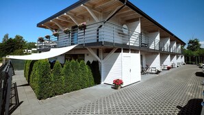 Un edificio de varios pisos con un balcón, una zona de estar al aire libre techada y un camino pavimentado.