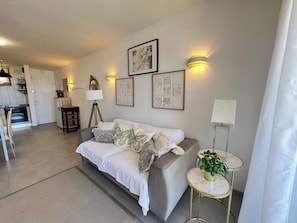 Ein modernes Wohnzimmer mit einer Couch, einem kleinen runden Tisch mit einer Pflanze und einer Küche im Hintergrund.
