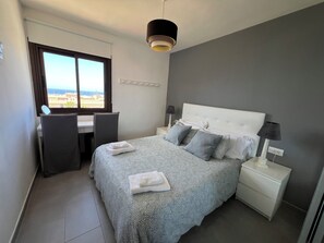 Ein Hotelzimmer mit Bett, Schreibtisch, Stuhl, Nachttisch, Lampe und Fenster mit Blick.