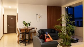 A living room with a dining table, a sofa, a potted plant, and a wall-mounted TV.