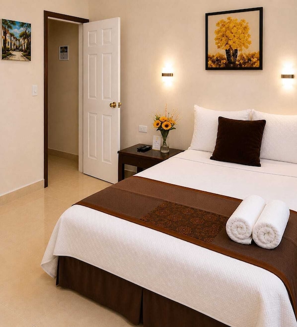 A hotel room with a bed, a nightstand, a vase with flowers, and a painting on the wall.