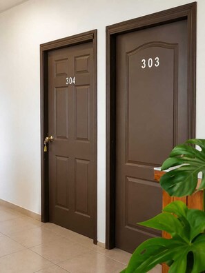 Two brown doors with numbers 304 and 303, a potted plant, and a tiled floor.