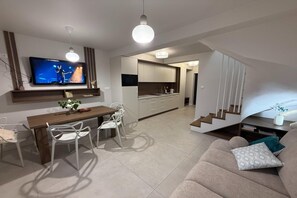 A modern living room with a flat-screen TV, dining area, kitchen, and staircase. - Half of a holiday home with a large garden (Slajszewo)