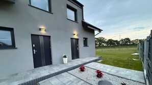 Un bâtiment moderne à deux étages, doté d’un toit plat, de grandes fenêtres et d’un patio dallé agrémenté de plantes décoratives.