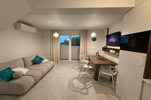 Una sala moderna con sofá, mesa de comedor, sillas, televisor de pantalla plana y microondas.