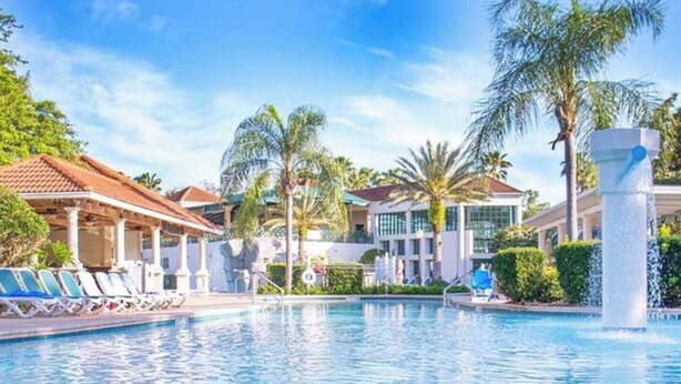 A swimming pool with lounge chairs, palm trees, and a building with a tiled roof. - Luxury 3BR Resort Villa w/ Jacuzzi Near Disney (Kissimmee)