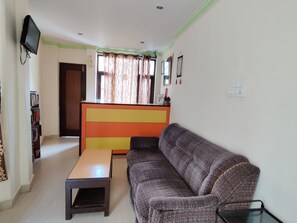 Una sala de estar con un sofá, una mesa de centro, un televisor y una estantería.