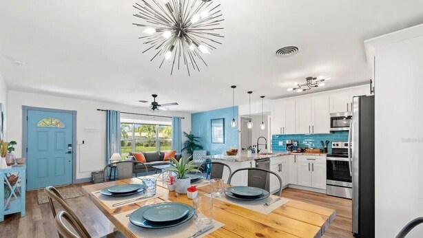 Una cocina moderna con armarios blancos, una isla central y un comedor con una mesa de madera para cuatro.