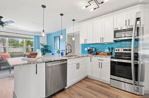 Eine moderne Küche mit weißen Schränken, einem Edelstahlbackofen und einer blauen Spritzschutzwand.