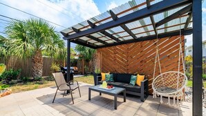 Un patio al aire libre con una zona de estar techada, una mesa y un sillón colgante.