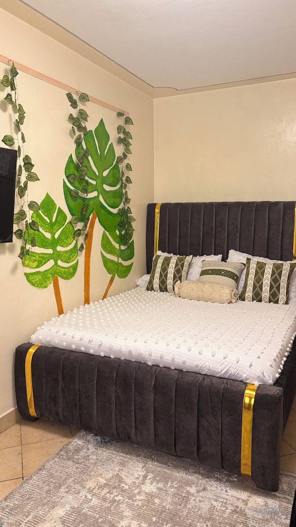 A bed with a dark headboard, white bedding, and decorative pillows. - Studio in south b near airport (Nairobi)