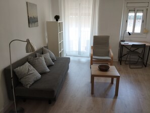 A living room with a sofa, a table, a chair, a lamp, a bookshelf, and a window. - Apartment in Barcelona near the Boqueria Market (Las Ramblas) (Barcelona)