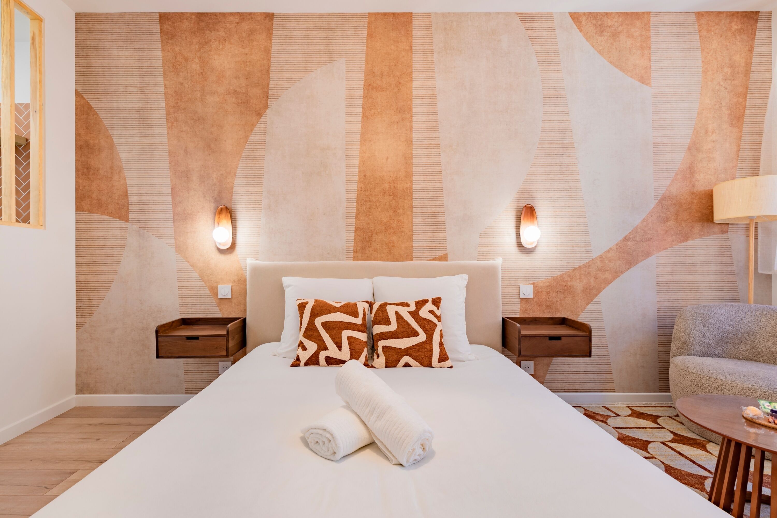 Ein Hotelzimmer mit einem großen Bett, zwei Nachttischen, einem Beistelltisch, einem Sessel und einer Wandleuchte.