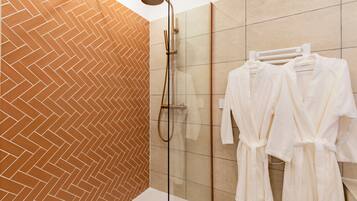 Un baño moderno con un patrón de baldosas en espiga, ducha con cerramiento de vidrio y batas blancas colgadas en un perchero.
