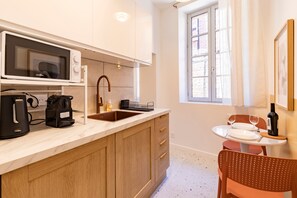 A kitchen with a microwave, coffee maker, sink, and a dining area with a table and chairs. - Studio Balnéo - L'Idylle Albigeoise - Appt pour 2 en centre-ville (Albi)
