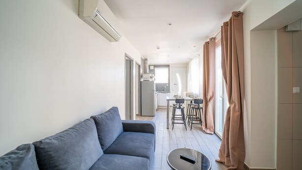 Ein modernes Wohnzimmer mit einer Couch, einem kleinen Tisch und einer Küchenzeile im Hintergrund.