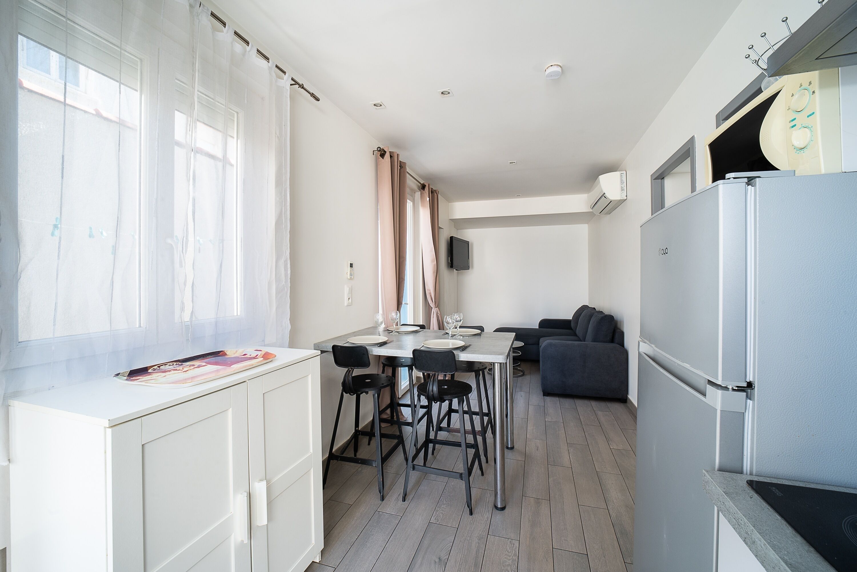 A modern kitchen with a dining area, white cabinetry, and a grey refrigerator.