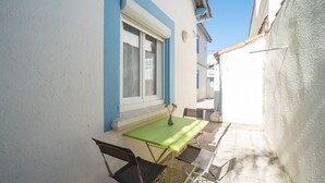 Eine kleine Außenveranda mit Tisch und Stühlen, ein Fenster mit Vorhang und eine blaue und weiße Wand.