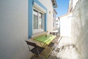 Eine kleine Außenveranda mit Tisch und Stühlen, ein Fenster mit Vorhang und eine blaue und weiße Wand.