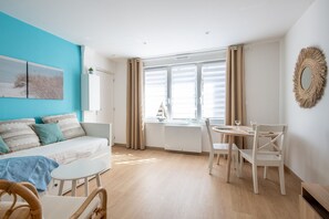 Ein modernes Wohnzimmer mit Sofa, Esstisch, Stühlen, einem Fenster mit Vorhängen und einem Wandspiegel.