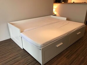A compact bed with a storage drawer underneath, a bedside table with a lamp, and a wooden floor. - La Pause courseullaise - Joli studio proche plage (Courseulles-sur-Mer)