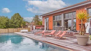 Una piscina con lettini, un pontile in legno e un edificio con ampie finestre.
