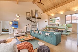 Ein modernes Wohnzimmer mit Wendeltreppe, einer grünen Sofagarnitur, einem Essbereich und einer Küche.