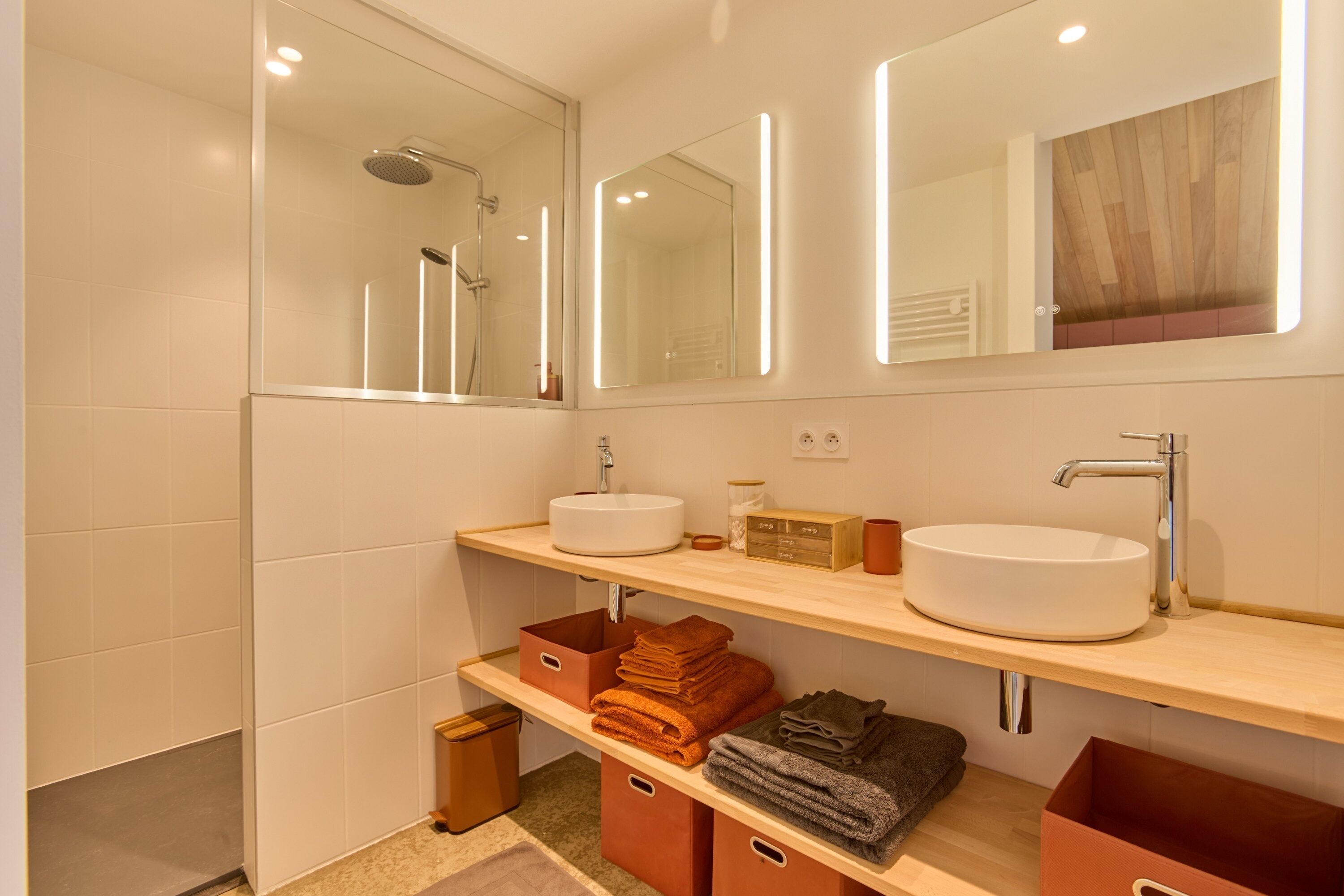 A modern bathroom with two sinks, a shower, and a mirror with integrated lighting.
