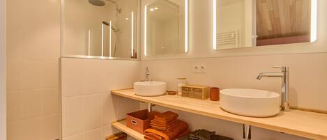A modern bathroom with two sinks, a shower, and a mirror with integrated lighting.