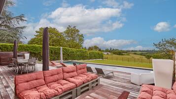 Une terrasse en bois avec un canapé rouge doté de coussins, une piscine et une vue sur un paysage verdoyant.